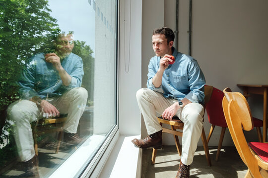 Businessman Looking Out Of Office Window Eating Apple