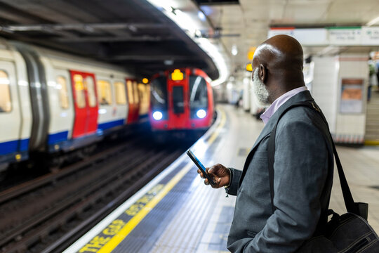 Businessman with smart phone looking at subway train arriving at station