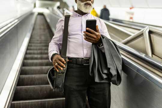 Senior Businessman With Suit And Mobile Phone Carrying Laptop Bag On Escalator