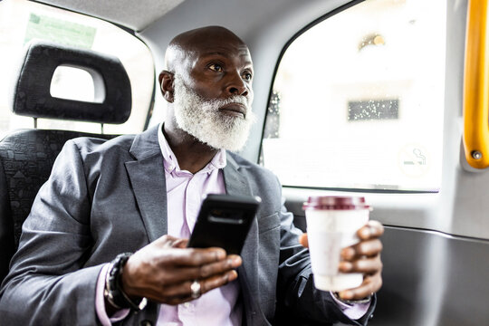 Senior passenger with smart phone having coffee in taxi