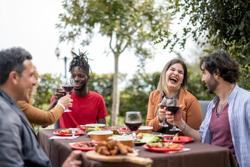 Happy people having good times while eating food and drinking wine in the garden, diversity and mixed age range concept