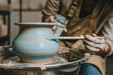 Hand's of potter painting pot on pottery wheel at workshop