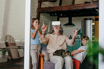 Grandfather wearing VR glasses having fun with grandchildren at home
