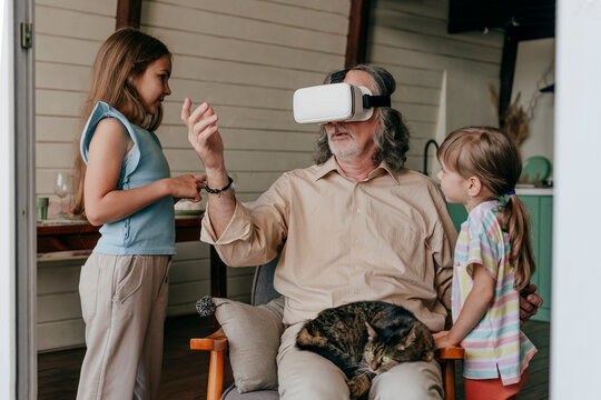 Grandfather wearing virtual reality simulator gesturing by grandchildren at home