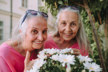 Portrait of senior women twins with flowers outdoor in city park.