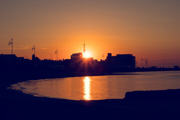 Fototapeta premium Silhouette of a town buildings by the ocean at sunrise. Warm orange color. Galway city, Ireland. Calm and peaceful mood.