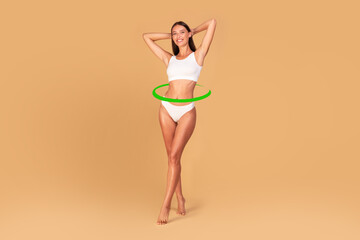 Slim young woman in underwear posing on beige studio background, green circle arrows around waist,...