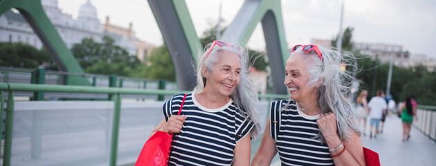 Happy senior twins in same clothes walking in city, returning from shopping.
