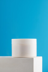 Mockup of a white jar with nourishing face and body cream on a pedestal on a blue background. Skin care.