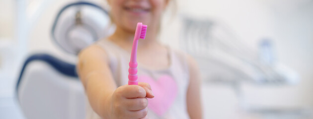 Close-up of little girl holding pink tootbrush, concept of children oral hygiene,prevention and dental health.