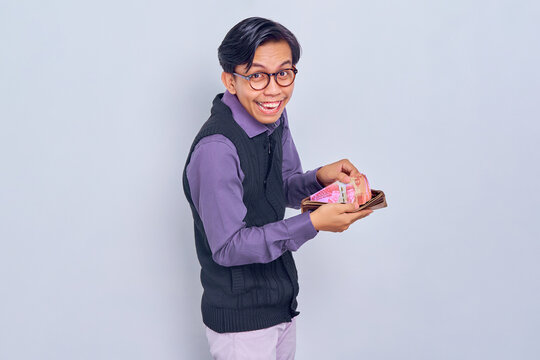 Portrait of excited young Asian man wearing shirt showing wallet with rupiah cash money isolated on white background