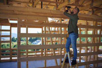 Construction worker working with screwdriver on wooden frame, diy eco-friendly homes concept.