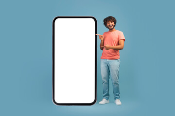 Cheerful eastern guy pointing at big smartphone with empty screen