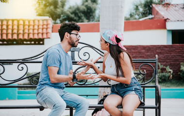 Obraz premium Man arguing with his girlfriend sitting in a park. Young couple arguing sitting on a park bench, Concept of aggressive couples in the park. Upset couple arguing on a park bench