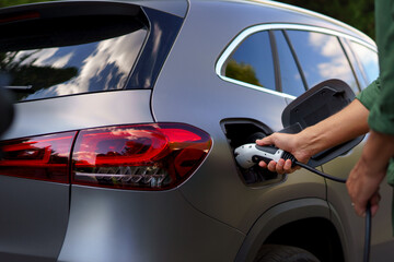 Man holding power supply cable at electric vehicle charging station, closeup