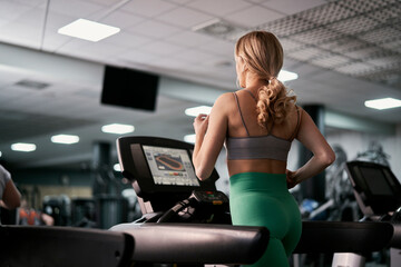 Rear view of caucasian woman running on treadmill at fitness center