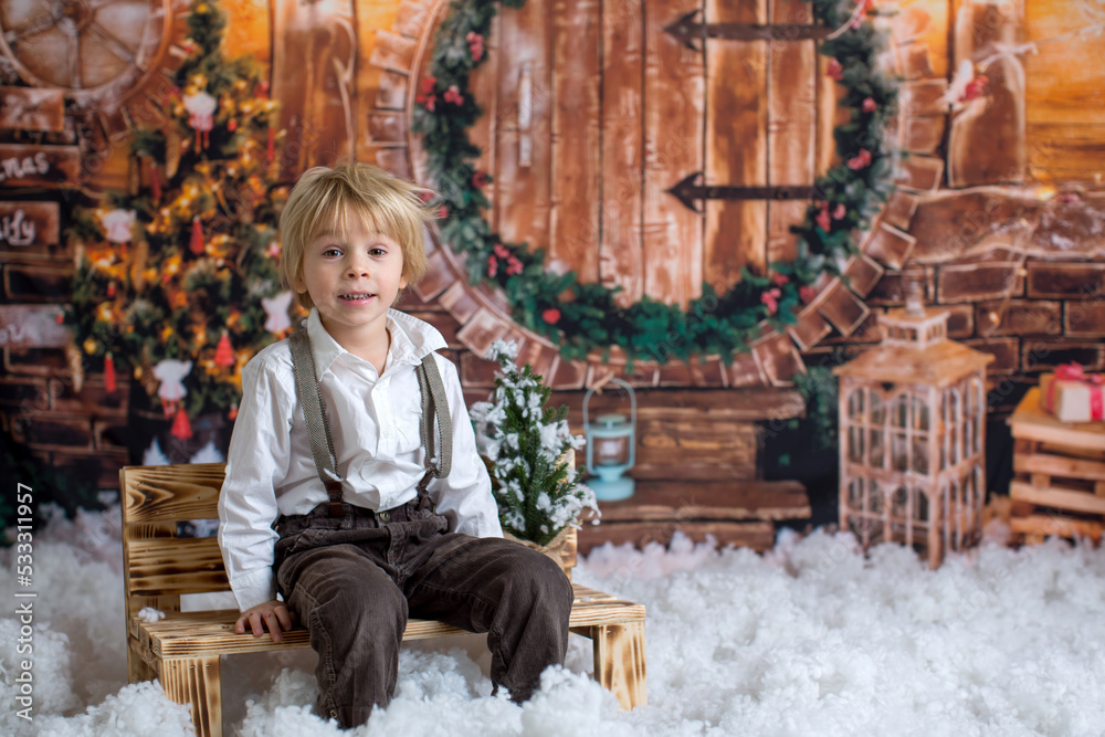 Sticker Cute fashion toddler boy, playing in the snow with teddy bear in front of a wooden cabin log