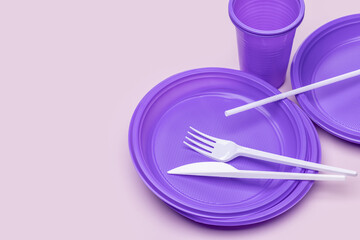 Disposable purple plates, glasses for drinks and cutlery on a pink background, top view. Plastic...