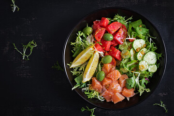 Ketogenic, keto or paleo diet lunch bowl with salted salmon fish, lemon, cucumber, olives, tomatoes, green lettuce salad and honey mustard dressing. Healthy food trend. Top view