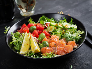 Ketogenic, keto or paleo diet lunch bowl with salted salmon fish, lemon, cucumber, olives, tomatoes, green lettuce salad and honey mustard dressing. Healthy food trend.