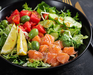 Ketogenic, keto or paleo diet lunch bowl with salted salmon fish, lemon, cucumber, olives, tomatoes, green lettuce salad and honey mustard dressing. Healthy food trend.