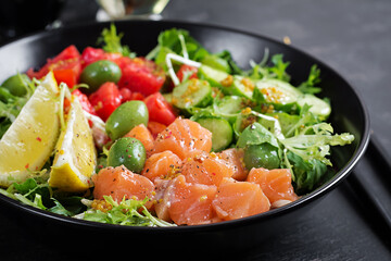 Ketogenic, keto or paleo diet lunch bowl with salted salmon fish, lemon, cucumber, olives, tomatoes, green lettuce salad and honey mustard dressing. Healthy food trend.