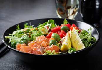 Ketogenic, keto or paleo diet lunch bowl with salted salmon fish, lemon, cucumber, olives, tomatoes, green lettuce salad and honey mustard dressing. Healthy food trend.