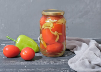 canned tomatoes and bell pepper preserves on wooden table next to fresh vegetables. homemade autumn season vegetable preserves.