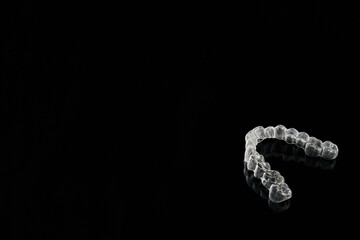 Transparent, invisible dental aligners or braces applicable to orthodontic treatment are placed on a black background.