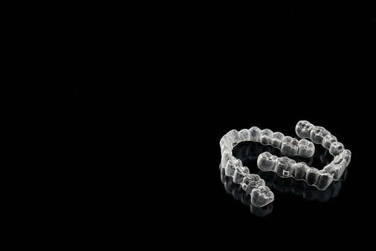 Transparent, invisible dental aligners or braces applicable to orthodontic treatment are placed on a black background.
