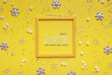 Merry Christmas greeting text in wooden frame with winter decoration on colored background.