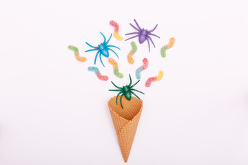 Halloween concept. Multicolored spiders, jelly candy worms and an ice cream cone on a white background. Flat lay, copy space, minimalism.