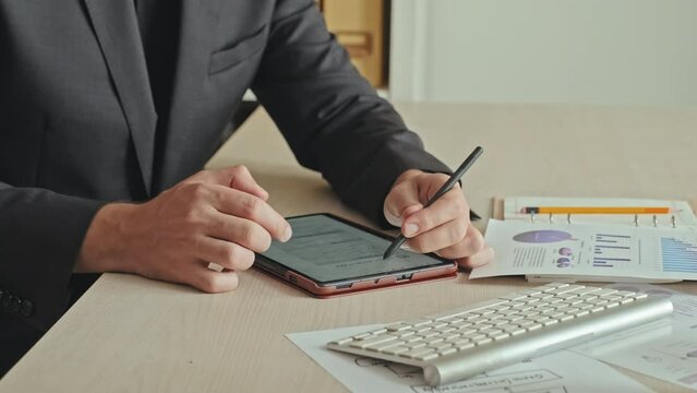 Cropped shot of unrecognizable entrepreneur filling out online application form on digital tablet while doing paperwork in office