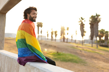 Happy gay man having fun holding rainbow flag symbol of LGBT community.