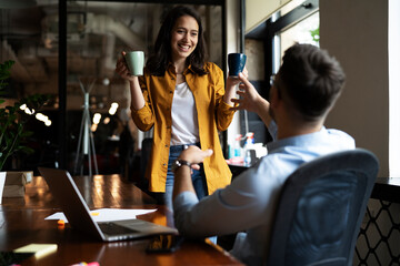 Colleagues laughing in office. Businesswoman and businessman drinking coffee..