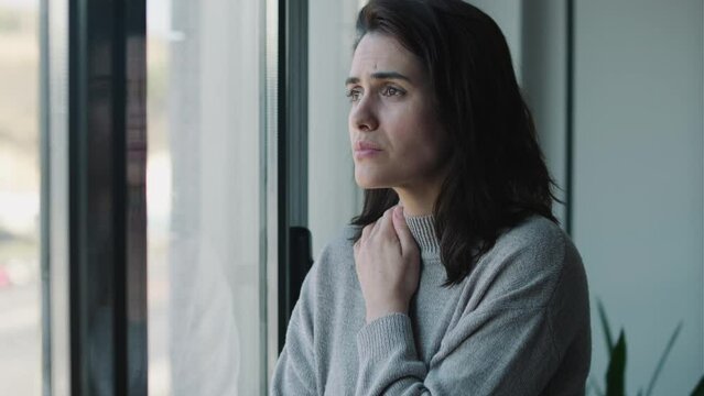 Video of depressed woman thinking while looking out window at home.