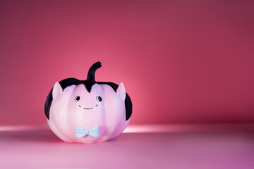 Halloween decorations on dark pink background. Funny and cute pink Vampire pumpkin with blue butterfly tie. Halloween card. Concept of entertainer, emcee for festive fall, autumn events. Copy space.
