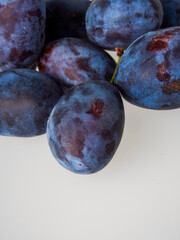 Black plums on wood background. Pile of black plums on a white serving plate. close up
