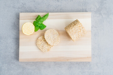 Top view raw Tempeh or Tempeh, made of fermented soybean seeds. Tempeh Slices on wooden board with herbs. Soya protein. Plant based meat. Healthy Cooking and eating. Go vegan. Flat Lay, copy space.