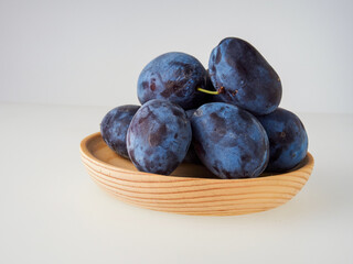 Black plums on wood background. Pile of black plums on a white serving plate. close up