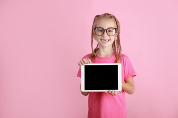 smiling funny child girl with tablet in hands on pink background. Caucasian school kid in glasses...