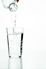 Detail of an unrecognizable man's hand pouring water into a crystal glass on a white background.