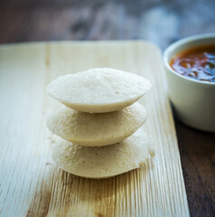 Rice idlis stacked on each other with bowl of sambar at the background. Indian food photography.