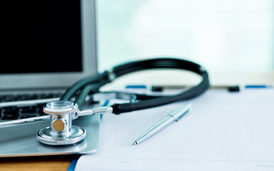 Stethoscope with clipboard and laptop on docotr desk
