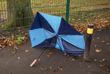 broken umbrella on path in autumn. Wind and weather concept. Damaged umbrella left on sidewalk