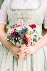 Close up shot of woman holding bridal flower bouquet in traditional dirndl dress in Germany