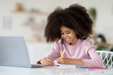 Adorable african american kid doing homework, using notebook
