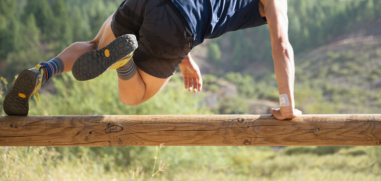 Participant in an obstacle course running, jump over wooden log obstacle