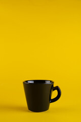 A black cup on a yellow background. Minimalism cup