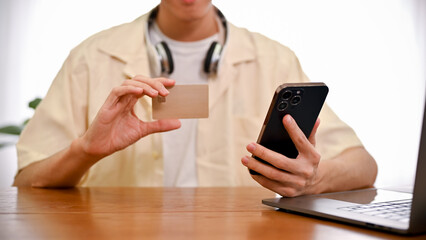 A young Asian man using smartphone and holding a credit card. Online payment, online shopping